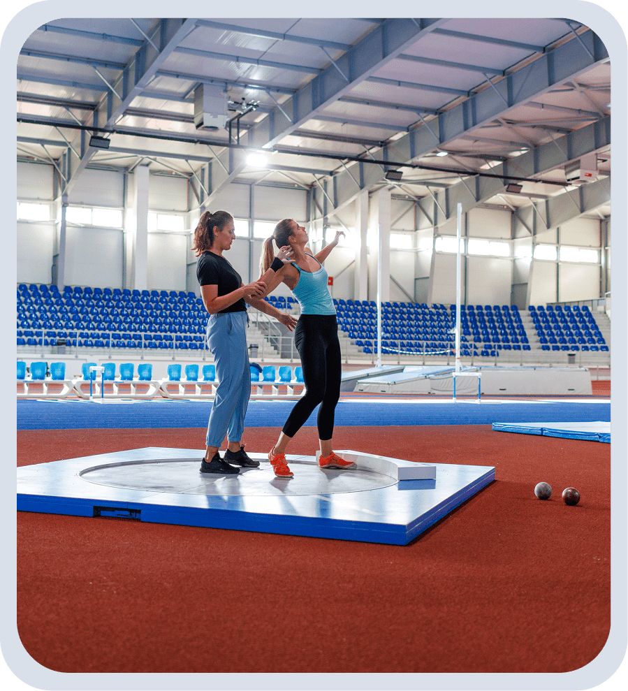 Two athletes practicing shot put indoors.